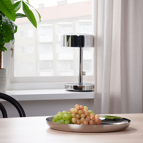 Bandeja de metal con uvas en una mesa de madera cerca de la ventana, lámpara en el fondo.