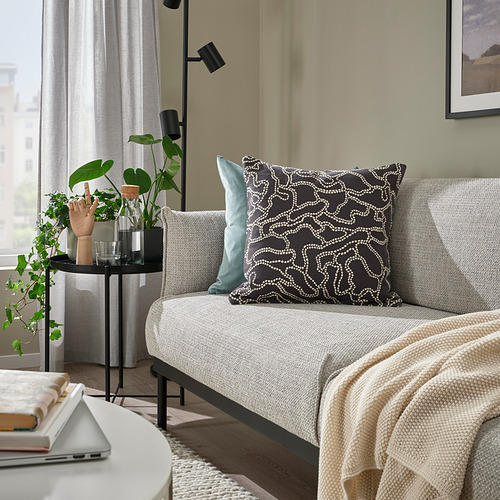 Acogedora sala de estar con cojín GULDFLY, sofá gris, almohadas decorativas, manta, plantas, computadora portátil, libros, cuadro enmarcado, lámpara.