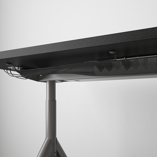 Escritorio negro con patas ajustables y red de gestión de cables debajo de la mesa.