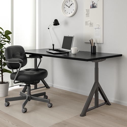 Configuración de escritorio y silla IDÅSEN con red de cable, ordenador portátil, taza y lámpara. Pizarra y reloj en el fondo.