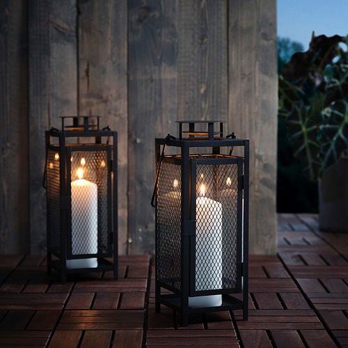 Dos faroles de metal negro con velas sobre cubierta de madera, iluminados, aptos para uso interior/exterior.
