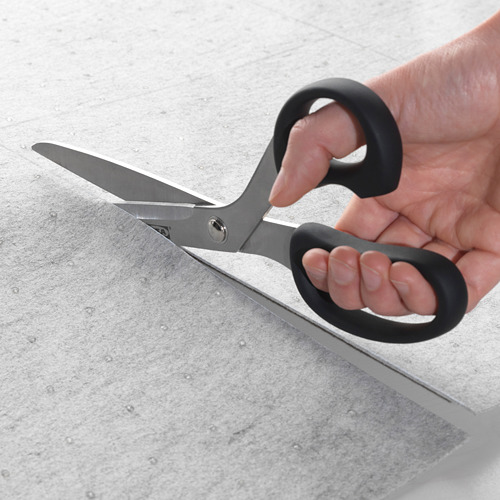 Persona que sostiene unas tijeras a punto de cortar un tapete de fieltro gris, que está diseñado para caber en los cajones para protección y evitar que los artículos se deslicen.