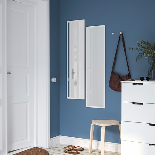 Una moderna habitación azul con un espejo vertical LILJETRÄD, una cómoda blanca, un bolso, una planta, un taburete y sandalias.