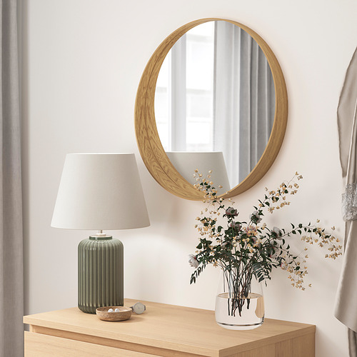 Decoración minimalista de la habitación: espejo redondo de madera, lámpara y jarrón blanco con flores secas sobre mesa de madera.