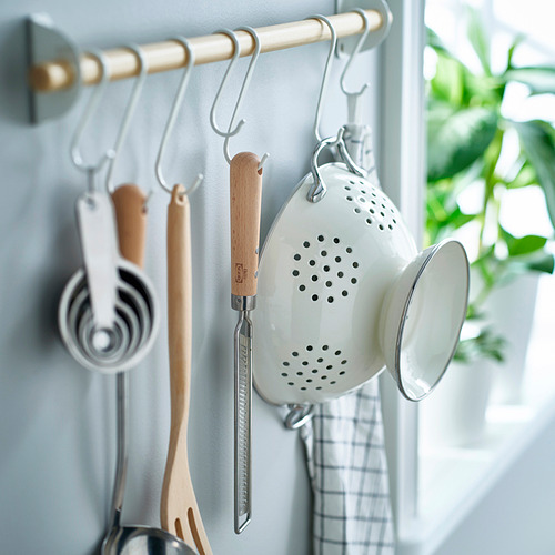 Utensilios de cocina colgados de ganchos. Se ve un rallador blanco con mango de madera, tazas medidoras, espátula de madera y un colador blanco.