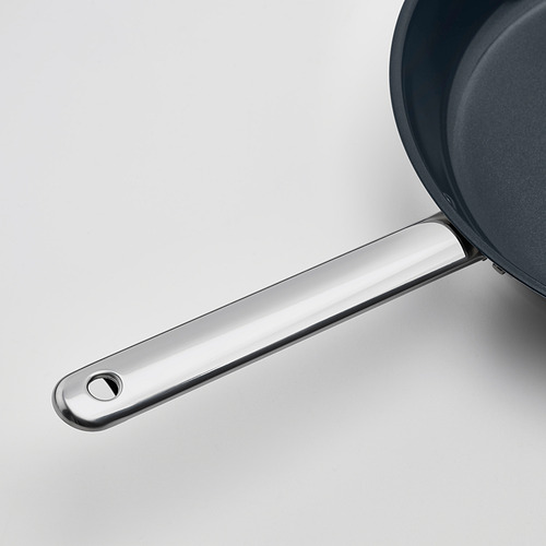 Primer plano de un moderno mango de sartén de acero inoxidable, unido a una elegante sartén antiadherente, que enfatiza su diseño de calidad.
