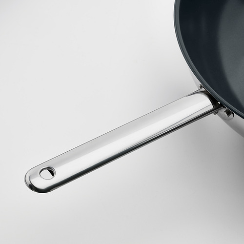 Brillante y moderno mango de wok fabricado en acero inoxidable, fijado de forma segura a una sartén antiadherente.