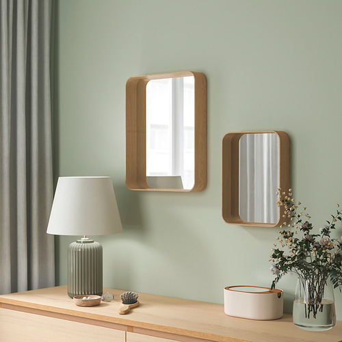 Dos espejos con marco de roble cuelgan de una pared verde, ventana reflectante, con decoraciones de mesa debajo.