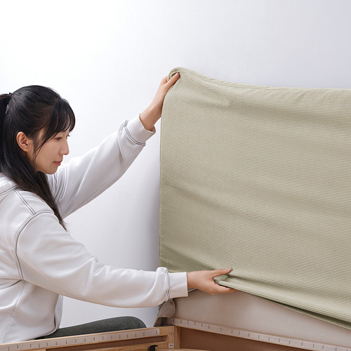 Una mujer ajustando un marco de cama beige con un cabecero acolchado. El marco tiene una funda extraíble que se puede lavar a máquina para facilitar la limpieza.