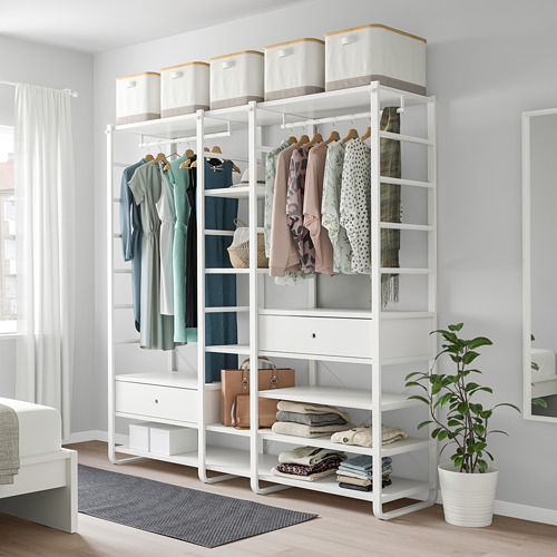Sistema de almacenaje ELVARLI blanco con estantes, cajones y ropa. Una planta añade naturaleza. Alto al lado de la cama.