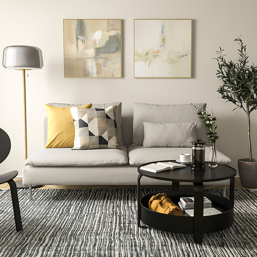 Sala de estar moderna con sofá SÖDERHAMN, blanco con almohadas estampadas, mesa de centro redonda negra, lámpara de pie y arte abstracto en las paredes.