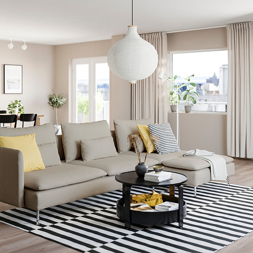 Sala de estar moderna con sofá SÖDERHAMN beige, almohadas amarillas, alfombra blanca y negra, mesa de centro redonda, grandes ventanales y lámpara colgante blanca.