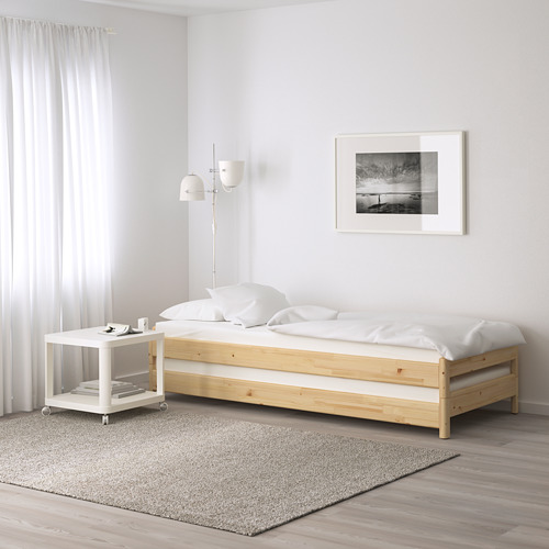 Dormitorio minimalista con cama de madera, colchón blanco, mesa pequeña, arte en blanco y negro, cortinas transparentes, ambiente sereno.