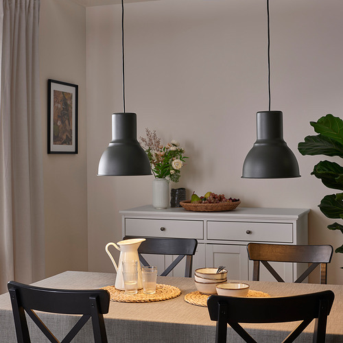 Lámparas colgantes negras sobre la mesa de comedor con sillas, que arrojan luz sobre la vajilla, las flores y el arte.