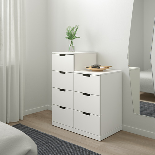 Cómoda blanca minimalista con seis cajones, planta y cuenco en el dormitorio, el espejo refleja el espacio.
