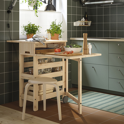 Cocina moderna con mesa de madera clara RESARÖ, acabado natural, plantas en macetas y armarios verdes.