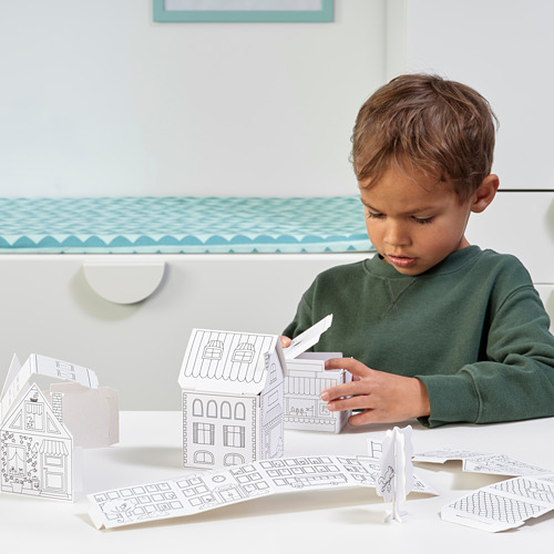 Un niño está haciendo manualidades con las plantillas de casas de cartón MÅLA, desarrollando la motricidad fina y la creatividad ensamblando y coloreando una pequeña ciudad.