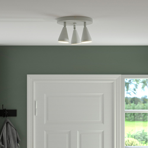 Tres proyectores de techo orientables, pertenecientes a la serie NÄVLINGE, montados sobre una puerta blanca en una sala verde, proporcionan una iluminación focalizada.