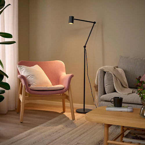 Acogedora sala de estar con silla color melocotón, sofá gris, mesa de madera, lámpara de pie negra y planta verde.