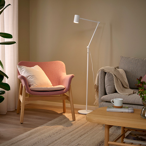 Acogedor salón con lámpara de pie NYMÅNE, madera clara, y tonos neutros. Silla rosácea, sofá gris, lámpara ajustable, mesa de centro de madera y alfombra.