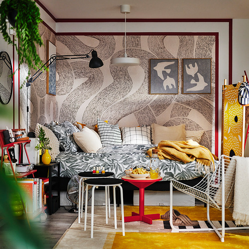 Cama de flores grises y blancas con manta amarilla y bandeja de desayuno. Acogedora habitación con alfombra amarilla y silla roja.