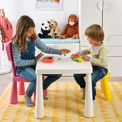 Los niños juegan con masa de colores en una mesa blanca, taburetes rosas. Animales de peluche cerca en un banco azul.