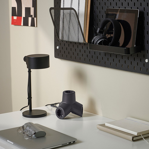 Una configuración de escritorio que muestra un enchufe de extensión negro de 4 vías, una lámpara y accesorios de computadora.