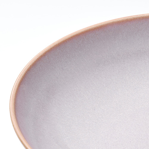 Primer plano de una elegante placa de gres esmaltado sobre una superficie blanca, que muestra una textura suave y uniforme y un sutil contraste entre el borde y el cuerpo.