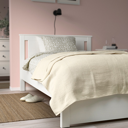 Un acogedor dormitorio con colcha INDIRA en color blanco roto y zapatillas beige.