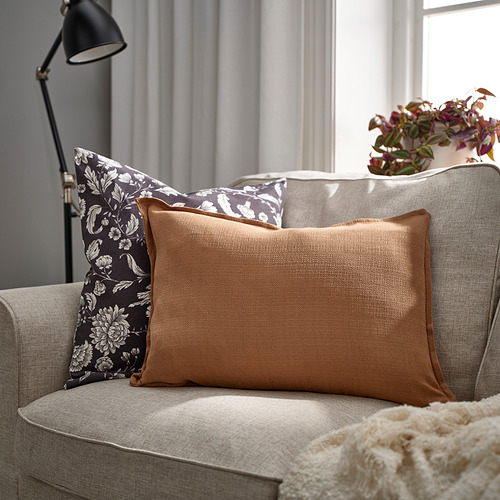 Cojín LAGERPOPPEL en sofá, en contraste con almohada floral y manta crema.