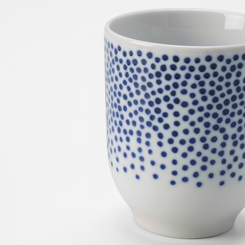Taza de porcelana con estampado de puntos blancos y azules, borde liso y acabado brillante. Diseño elegante y detallado.