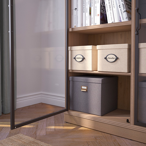 La vitrina con puerta de cristal exhibe libros y cajas, con asas metálicas y estantes de madera, aseguradas a la pared.