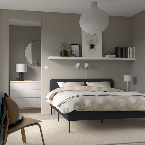 Dormitorio moderno con cama SLATTUM, edredón grande de lunares, decoración minimalista, iluminación acogedora y espejo de pared.