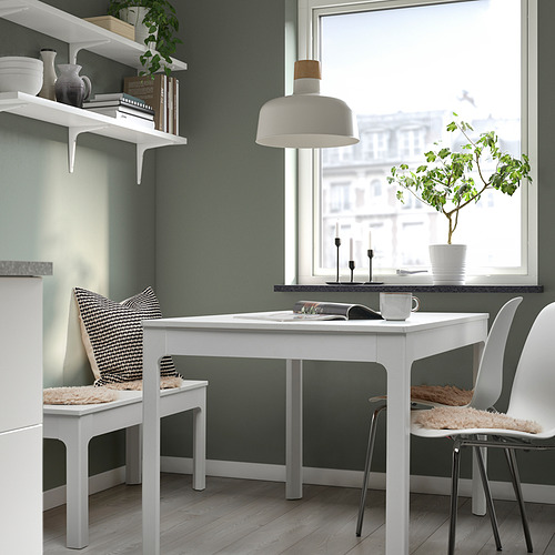 Acogedor espacio de trabajo con mesa blanca, dos sillas acolchadas, paredes verdes, lámpara y planta.
