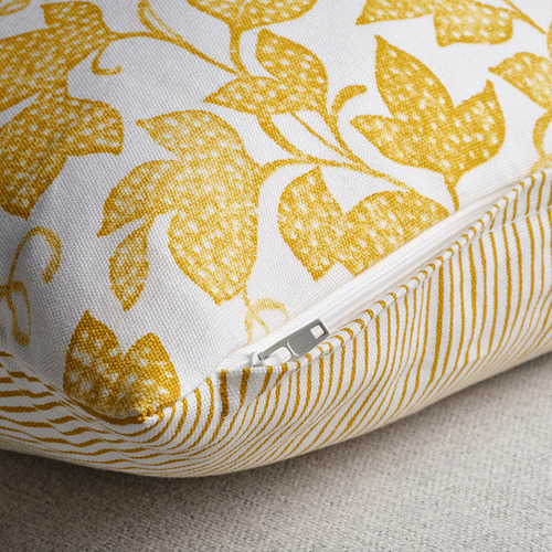 Almohada amarilla y blanca con un intrincado estampado floral, con una cremallera oculta en un lado.