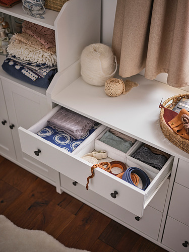 Un mueble de almacenaje HAUGA blanco con cajones abiertos y diversos textiles en la parte superior.