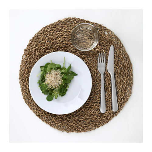 Un plato blanco con ensalada verde, vaso y utensilios sobre mantel individual tejido.