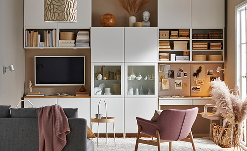 Unidad blanca BESTÅ con puertas de vidrio, tv, sofá, silla, mesa y flores.