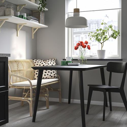 Comedor moderno con mesa de madera, sillas negras, banco estampado, ratán, cuero y lámpara colgante. Elementos esenciales de cocina en estantes.