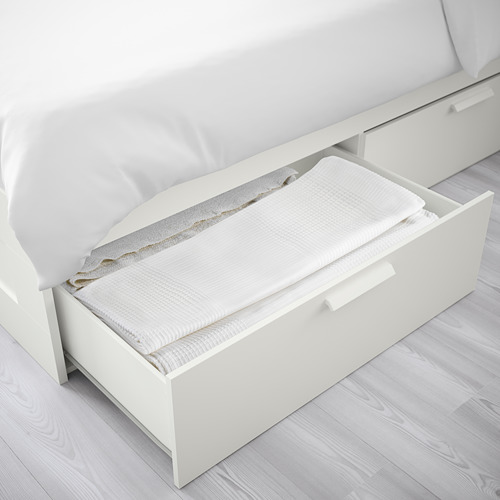 Cajón de cama blanco abierto con sábanas dobladas, parte de la serie BRIMNES de ikea.