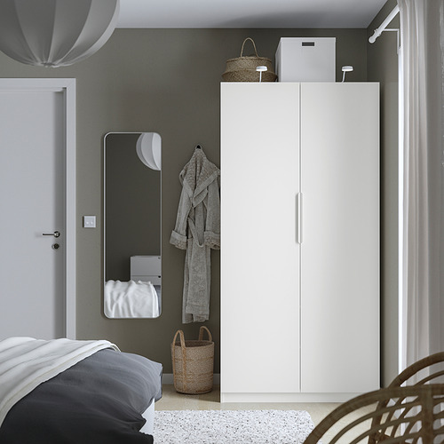 Dormitorio minimalista con un armario PAX blanco, un armario alto y delgado cerca de una cama, una pared gris, un espejo y una bata colgante.