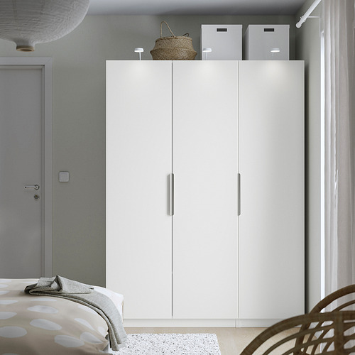 Dormitorio minimalista con gran armario blanco PAX, cortinas transparentes, puerta gris y cama con colchón de lunares.
