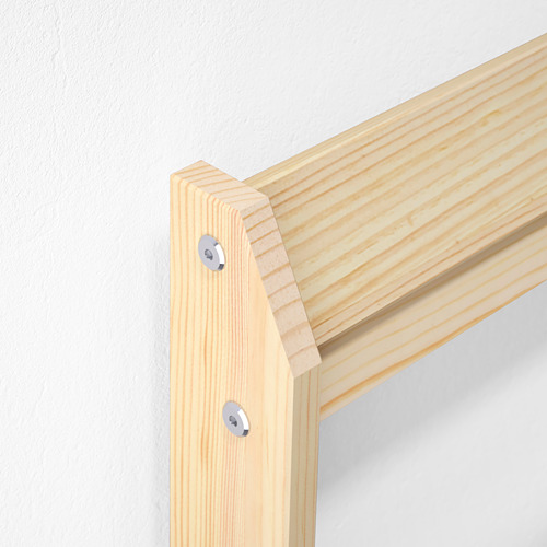 Primer plano de la junta de la estructura de la cama de madera robusta y bien recortada con herrajes transparentes contra una pared blanca.