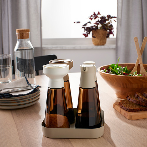 Moderna configuración de mesa con tarros de especias de vidrio marrón, que incluyen un molinillo de especias y una jarra con tapón de corcho. También hay una ensaladera de madera y platos.