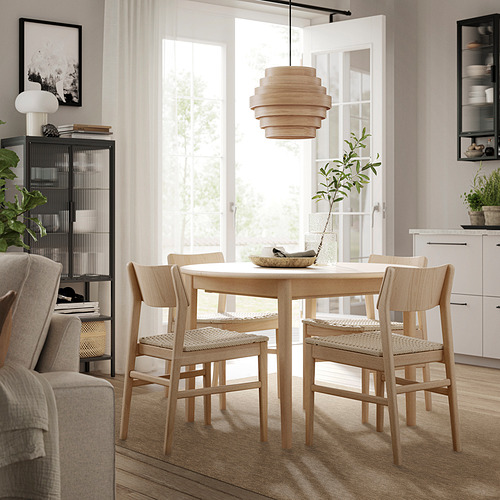 Comedor moderno con alfombra LÄTTBETONG, mesa y sillas de madera, sillón gris, estantería negra. Cálidos y acogedores, tonos claros.