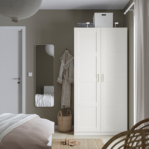 Dormitorio minimalista con armario alto blanco PAX y espejo de cuerpo entero junto a la cama.