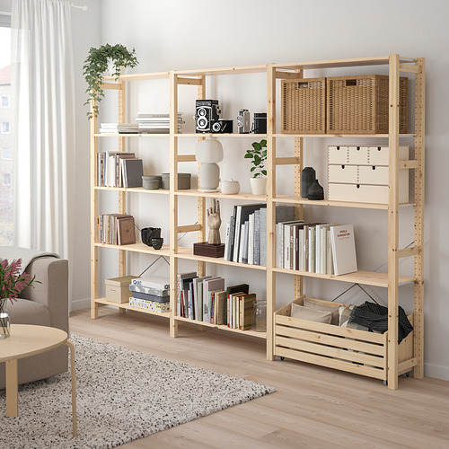 Estantería IVAR de madera natural, repleta de libros, cestas y artículos decorativos. Alto, rectangular, encaja bien con un sofá grande y una alfombra.