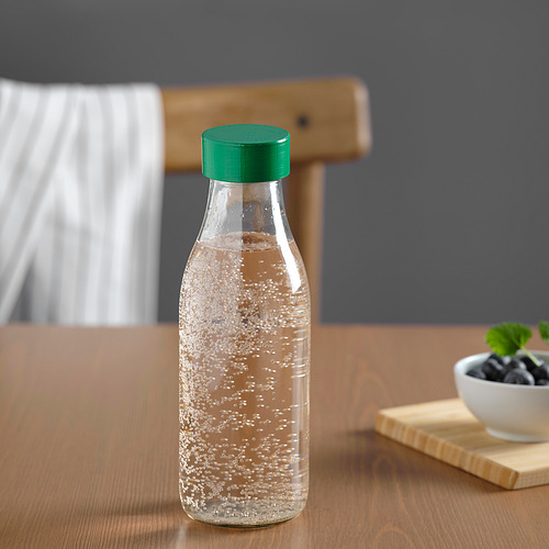 Botella de agua de vidrio transparente con tapa verde sobre mesa de madera.