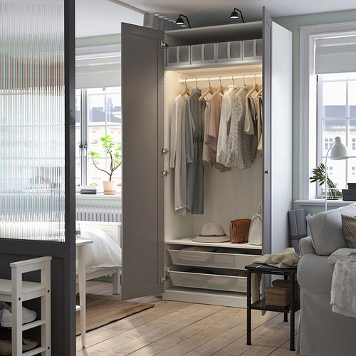 Open dark wardrobe displaying clothes, accessories, and shelves; lit interior, positioned next to window.