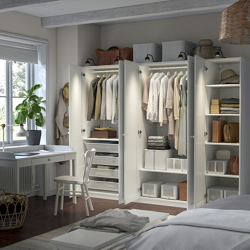 Dormitorio organizado con armarios blancos PAX. Estanterías con cajas blancas y ropa. Pequeño escritorio junto a la ventana.